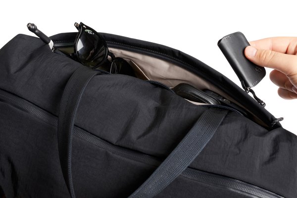 A hand lifting a tethered key fob from the Lite Duffel's exterior organization pocket