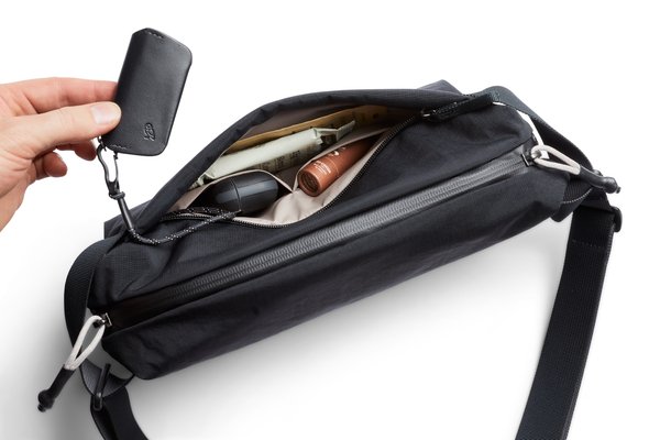 A hand lifting a key fob attached to the Lite Sling's key tether beside its open front pocket
