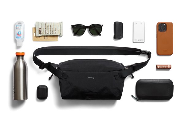 Black Bellroy Lite Sling beside a phone, sunglasses, bottle and other illustrative everyday items