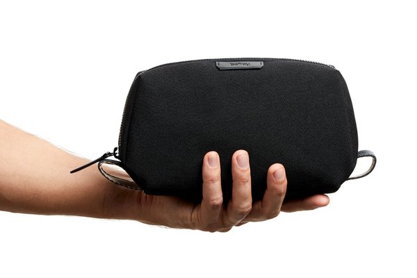 A hand holding the closed standard black Bellroy Toiletry Kit beneath its base