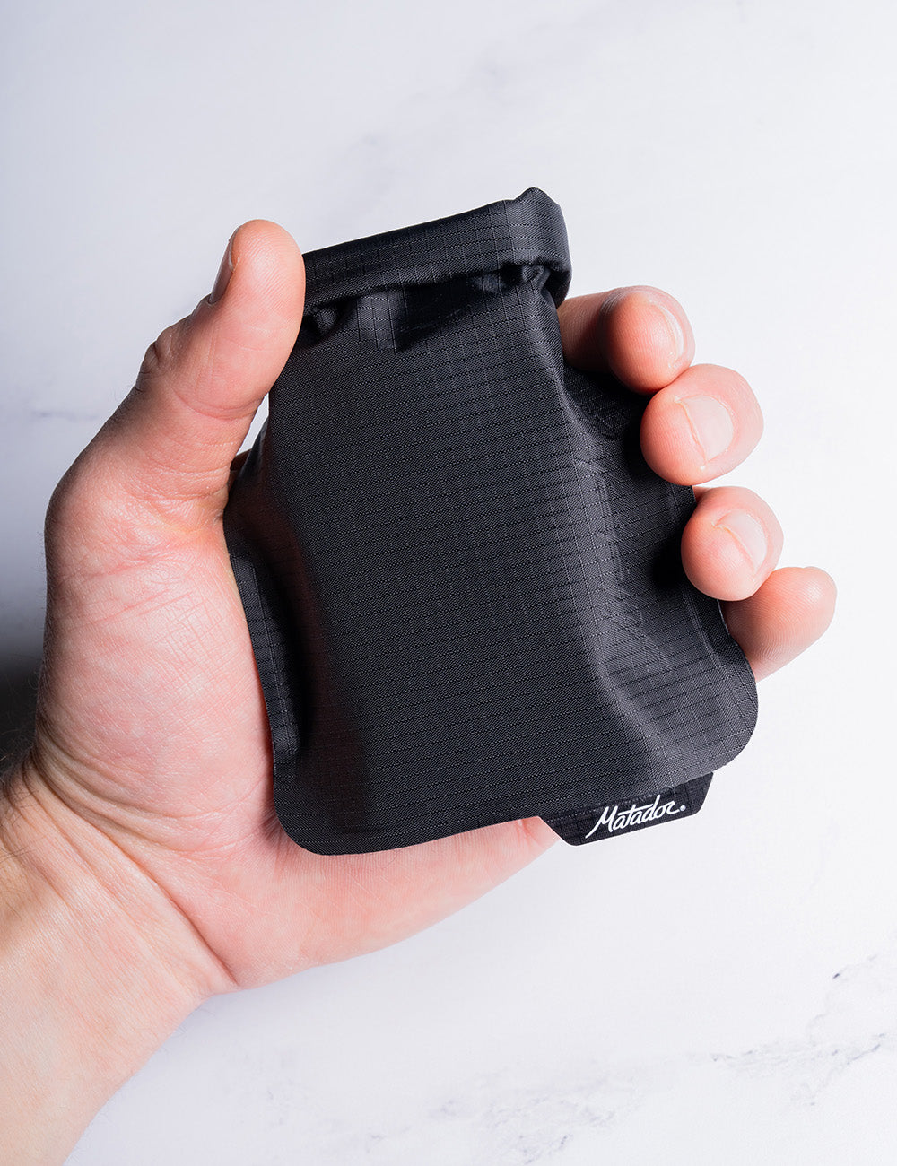 A hand holding the roll-top of the black Matador FlatPak V2