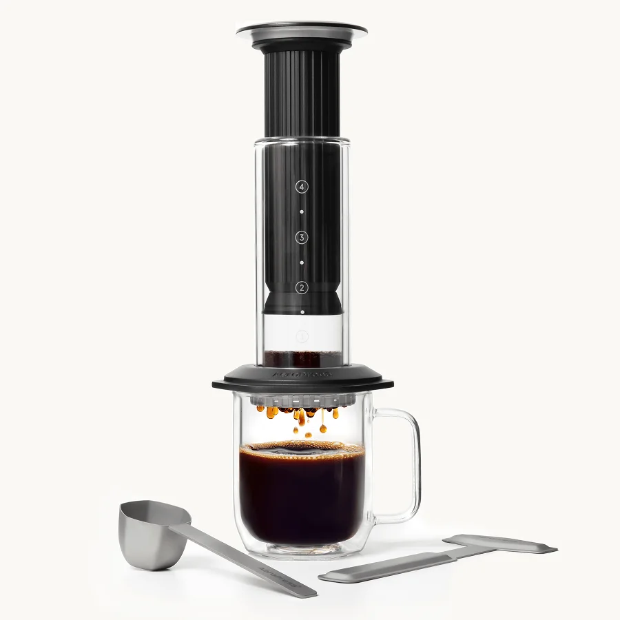 Black AeroPress Premium with scoop and stirrer; the photographed mug is a serving prop.