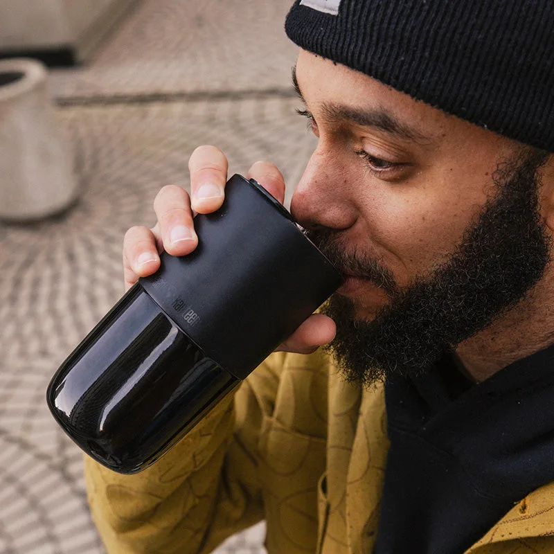 Black tumbler held upright while drinking.