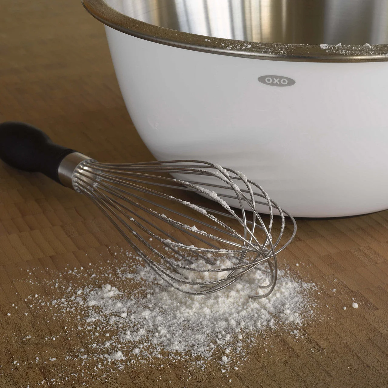 Whisk beside a mixing bowl in a staged baking scene.