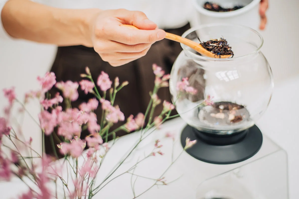 Adding loose leaves using a spoon; spoon is a styling accessory.