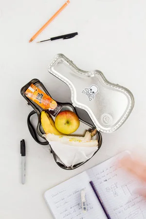 Open lunchbox in a tabletop scene; stationery, food and surrounding props are separate.
